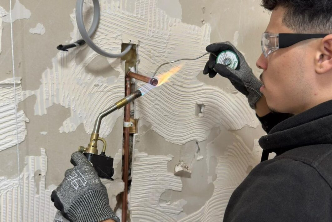 Man wearing googles doing work on a gas pipe with a blow torch.
