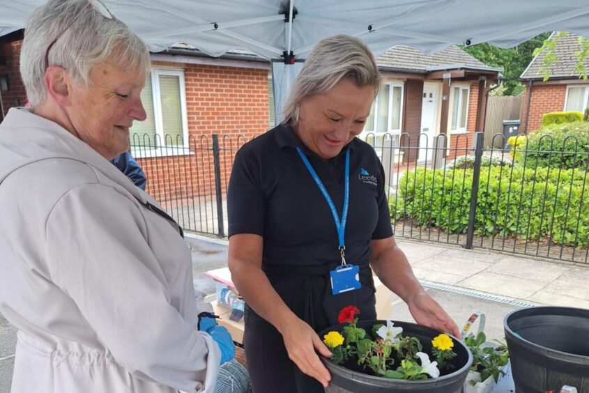 Two women stood under a gazebo smiling at a flower pot