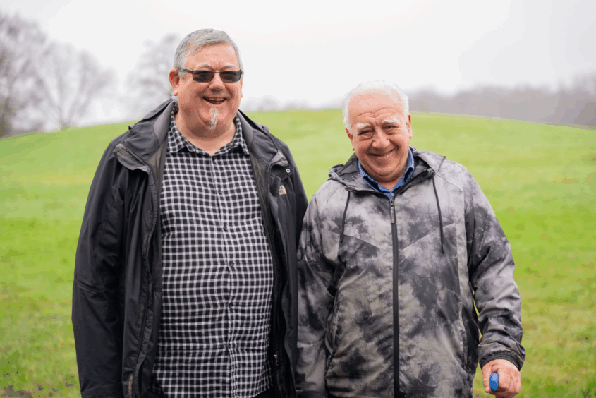 Two older men walking in the both. Both men are smiling. One man is walking with a stick.