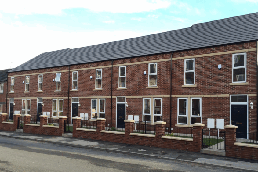 Street view showing a row of terraced houses in The Arthingtons. Each home has a front yard with a path up to the front door. There is a low wall and railings separating each yard from the pavement and road in the foreground.