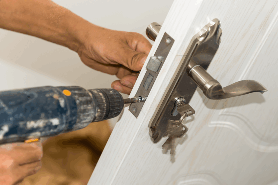 Close up of a lock being changed. A hand is holding a drill which is screwing in the lock. Another hand is supporting the door