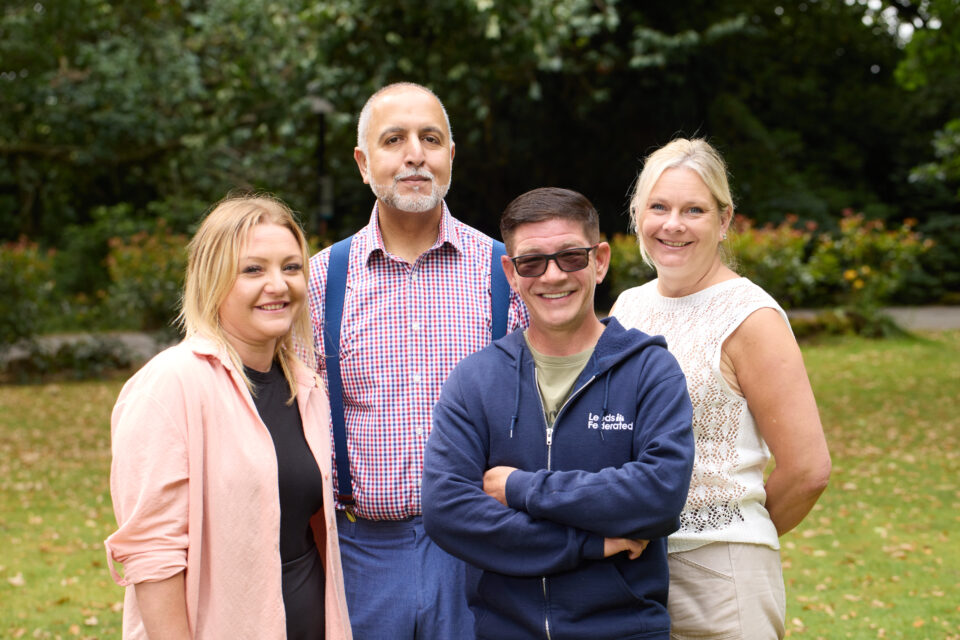 South team standing on a lawn together. They are smiling. There are trees in the background.