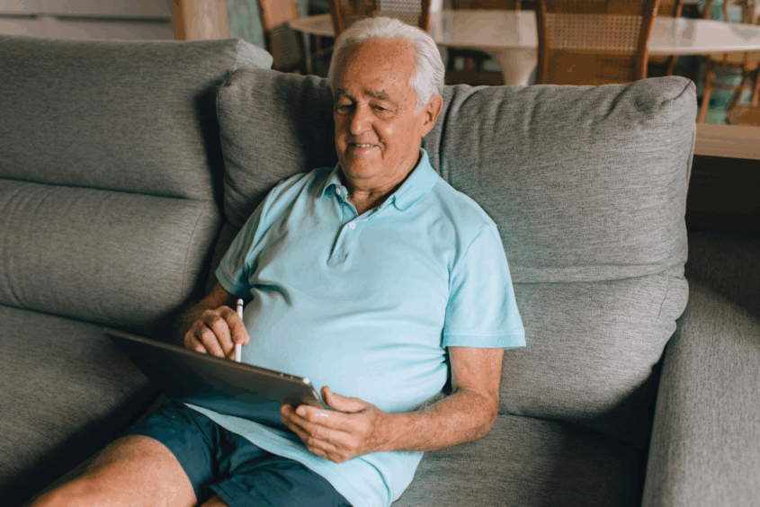 Older man sitting on the sofa. He is using a tablet.