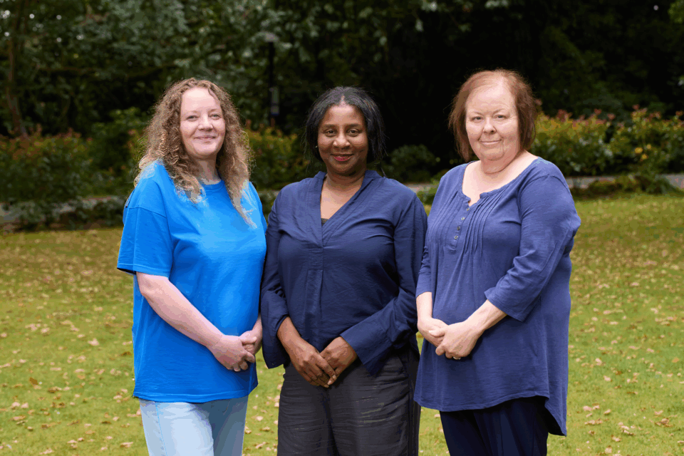 Central team standing on a lawn together. They are smiling. There are trees in the background.