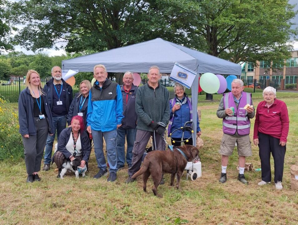 People stood in a line smiling at the camera in front of a gazebo. There is also a dog