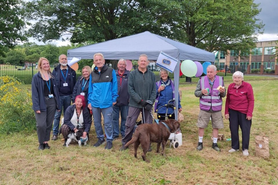 People stood in a line smiling at the camera in front of a gazebo. There is also a dog