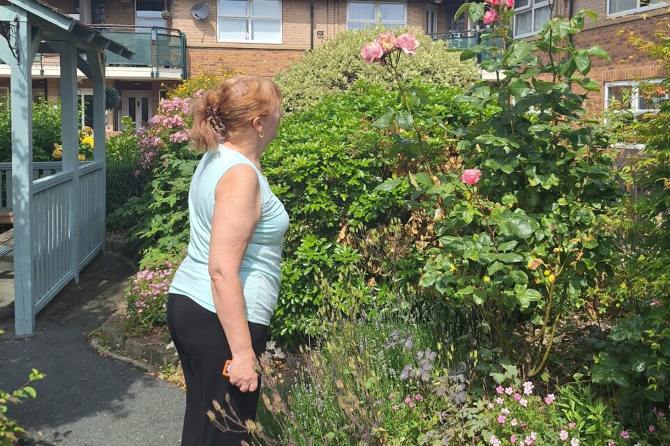 A woman stood in a garden looking to the side at flowers