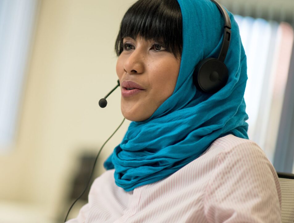 Woman wearing a headset as though she is working in a call centre. She is also wearing a hijab