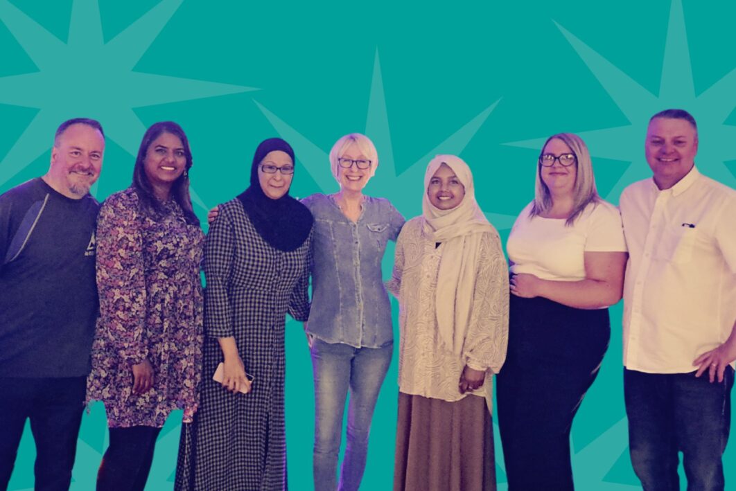 Team from MEL Research. 7 members of the team are standing in a line smiling.