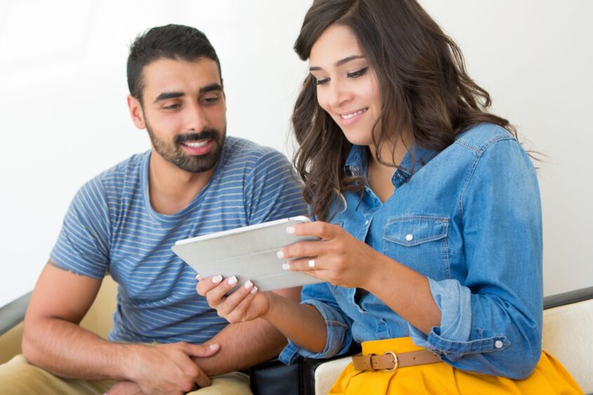 Couple sitting on the sofa looking at a tablet. Both are smiling.