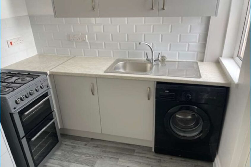 Completed kitchen showing white fitted cabinets and worktop, black washing machine and white metro wall tiles