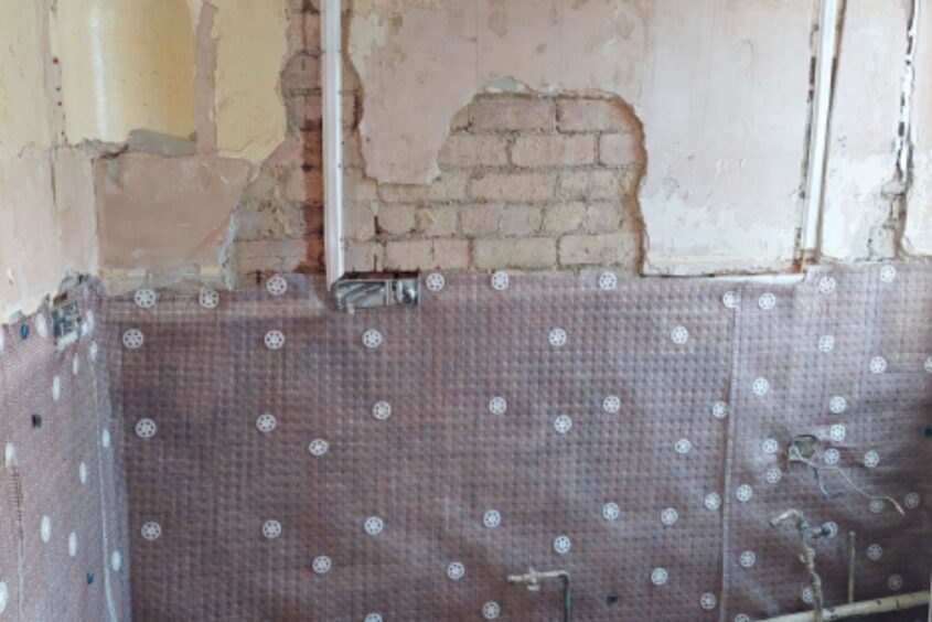 Installing damp-proofing in the kitchen. The top half of the wall is plastered, the bottom half has a damp-proof membrane attached to the wall