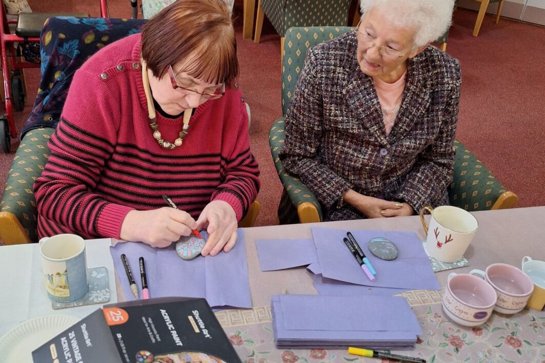 Two women painting pebbles at a table