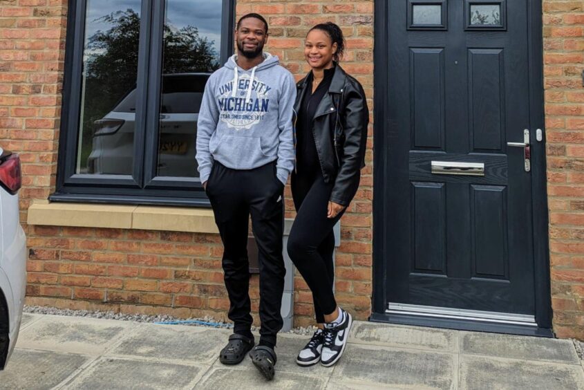 A couple standing outside their front door. They are both smiling