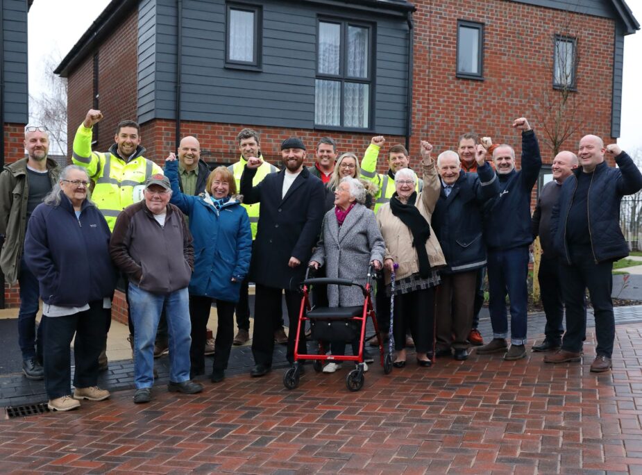 People stood in front of a new house, in a line smiling.
