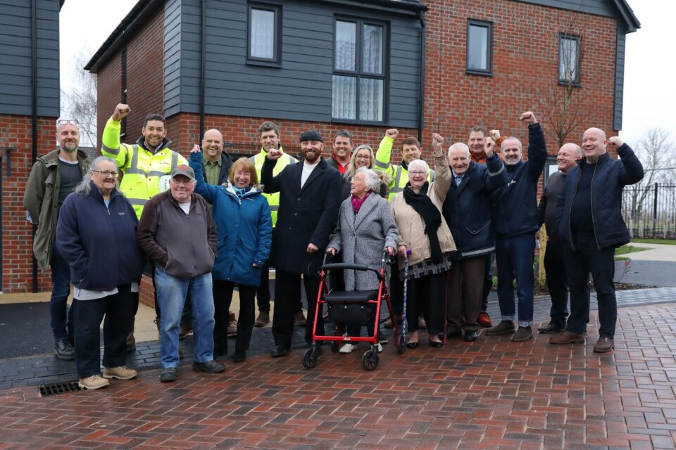 People stood in front of a new house, in a line smiling.
