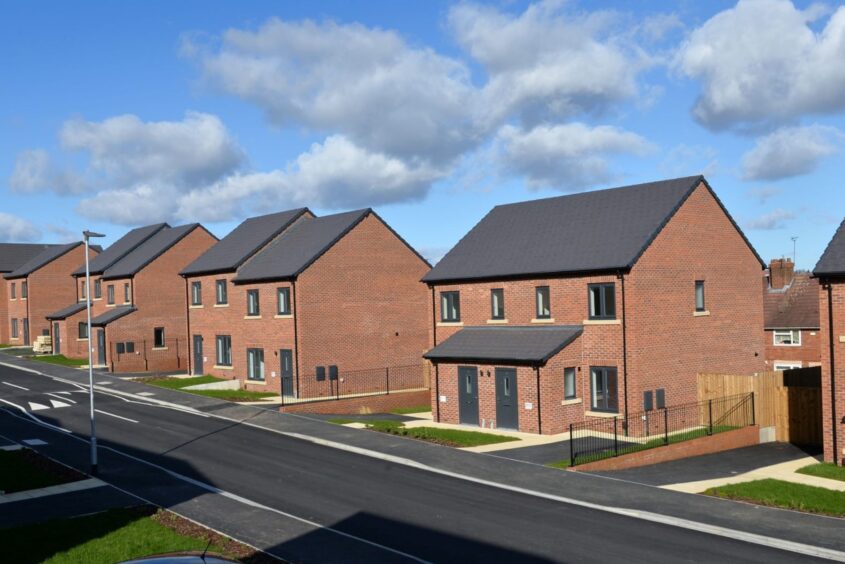 Row of semi-detached new build shared ownership homes. A road passes in front of the homes. It's sunny weather.