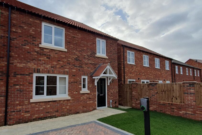 A row of red brick new build homes. The home in the foreground has a brick drive, small lawn area and electric car chargin point at the front