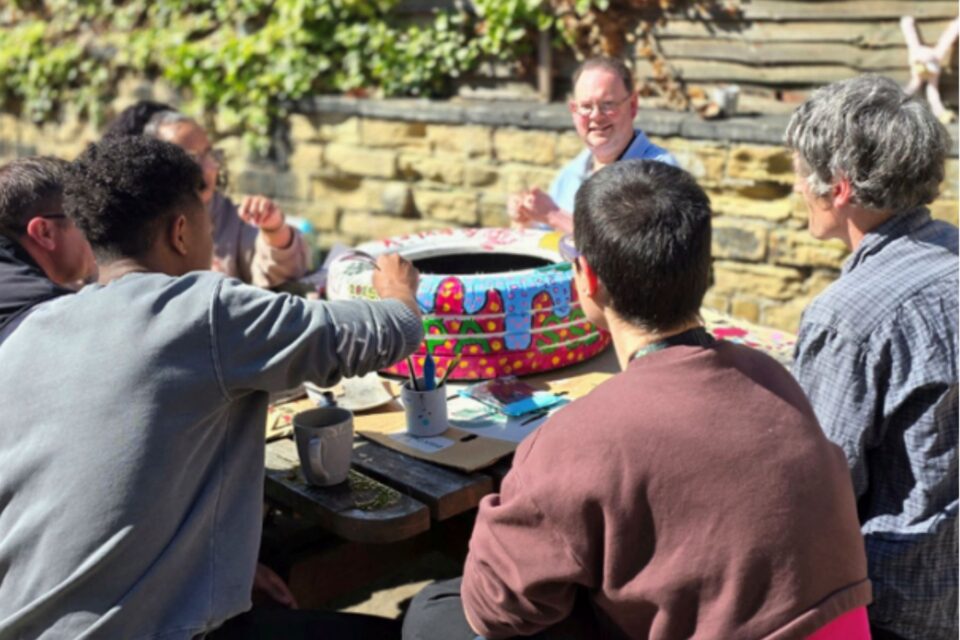 People sat round a table outside talking and doing painting