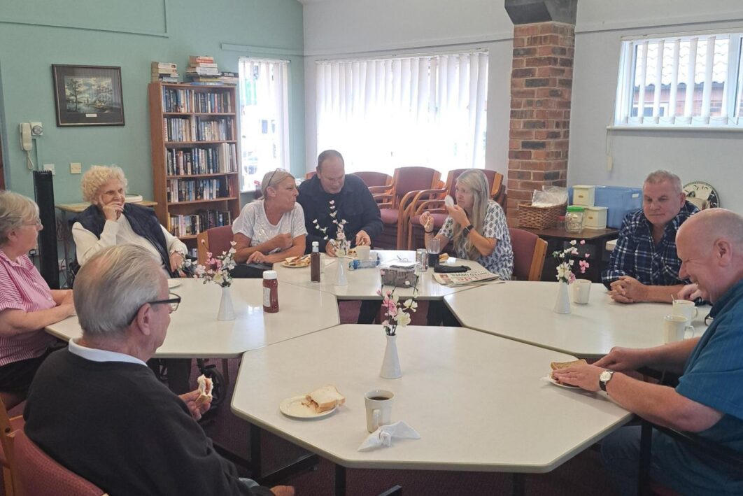 People sat round a large table eating bacon sandwiches and chatting