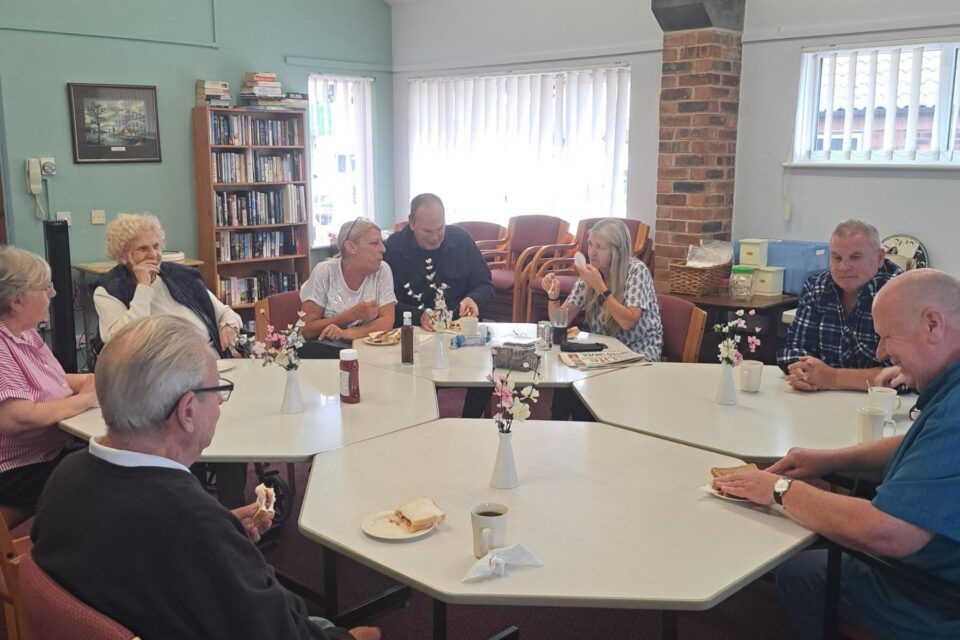 People sat round a large table eating bacon sandwiches and chatting