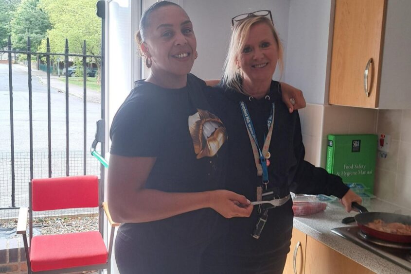 Two women stood in front of a kitchen counting smiling at the camera