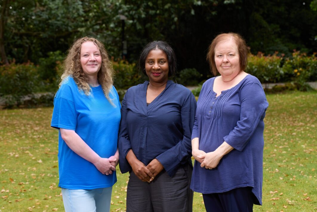 3 people stood together in a line smiling at the camera.