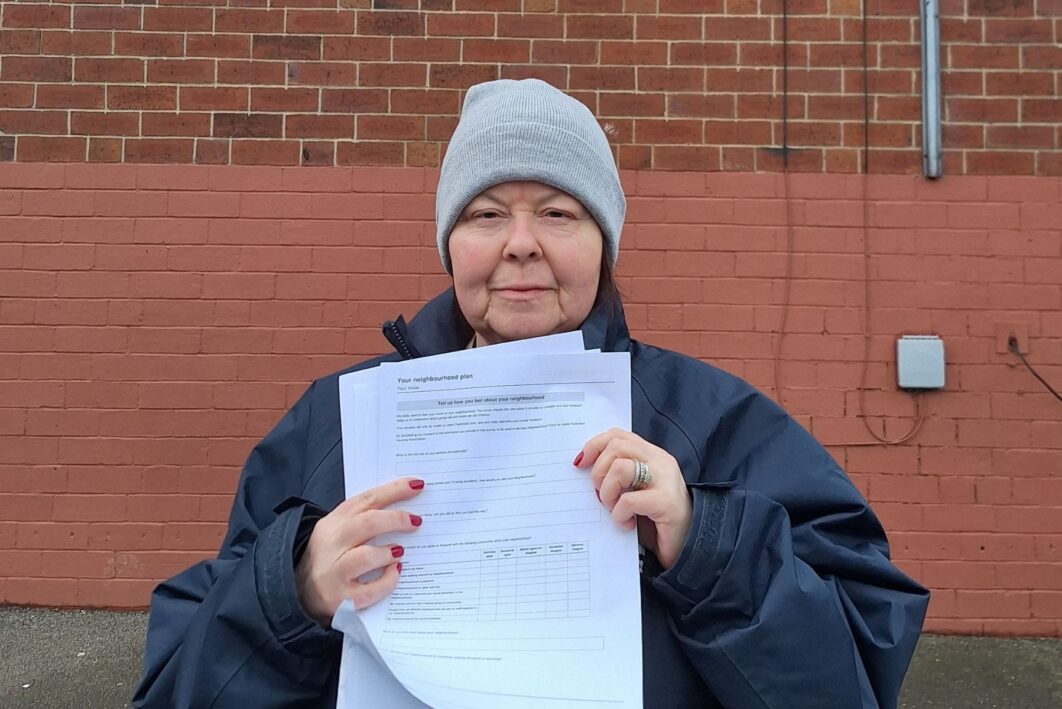 Picture of neighbourhood Officer Maggie stood in front of a wall of a house holding a form up at the camera.