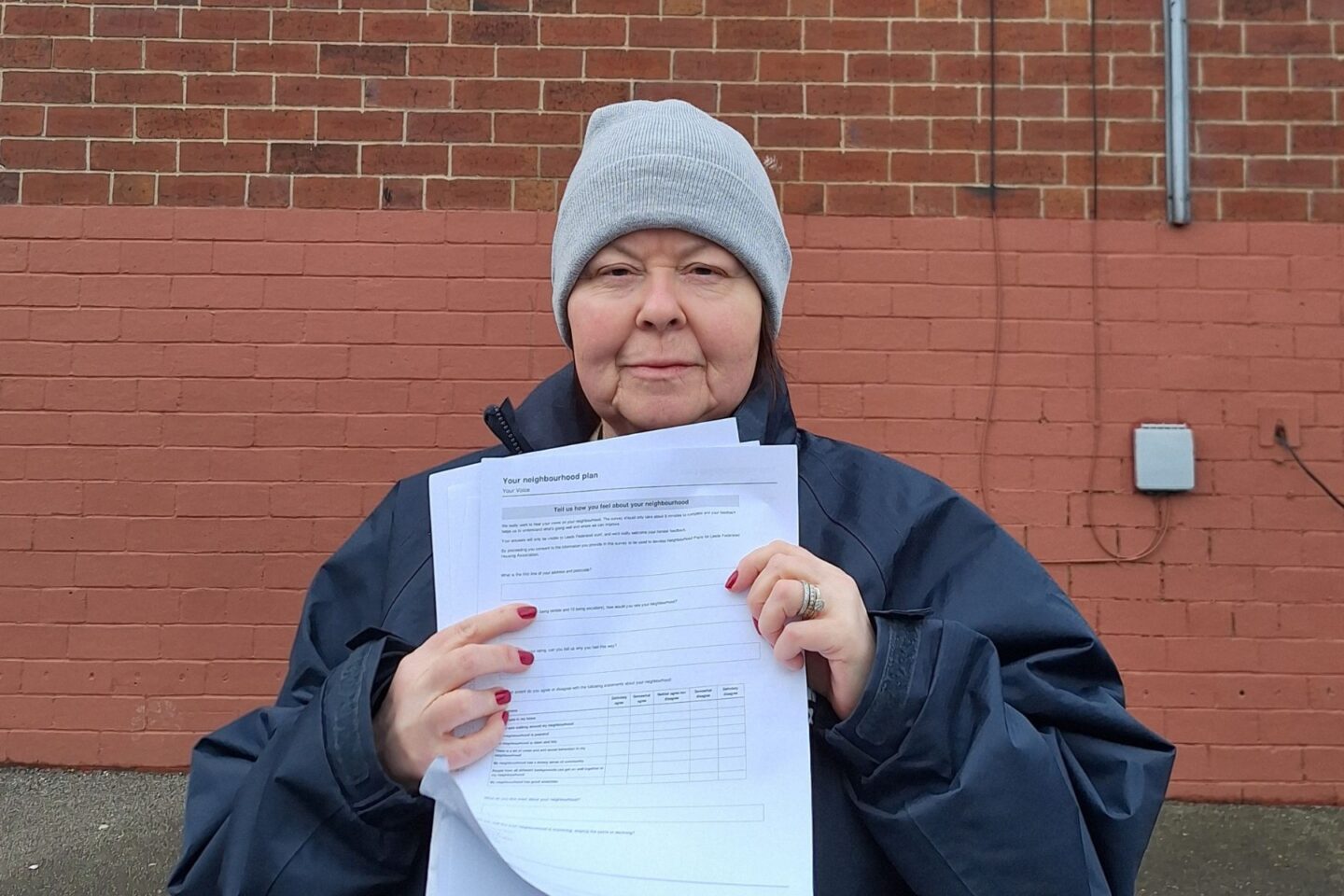Picture of neighbourhood Officer Maggie stood in front of a wall of a house holding a form up at the camera.