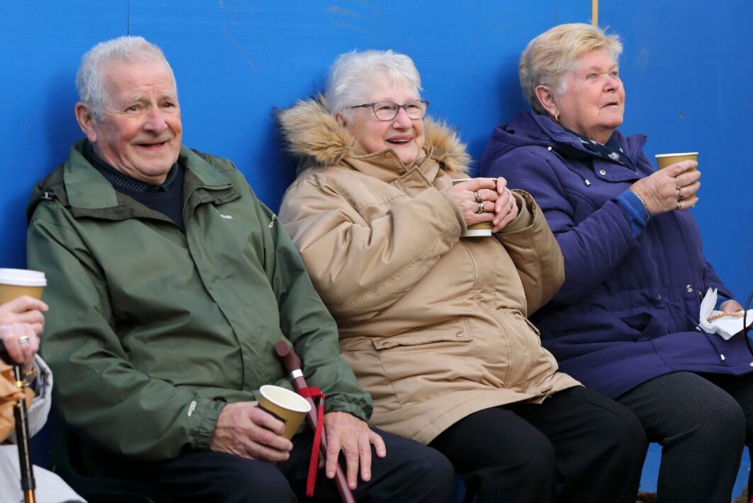 Three people sat together in coats. They are all holding coffee cups.
