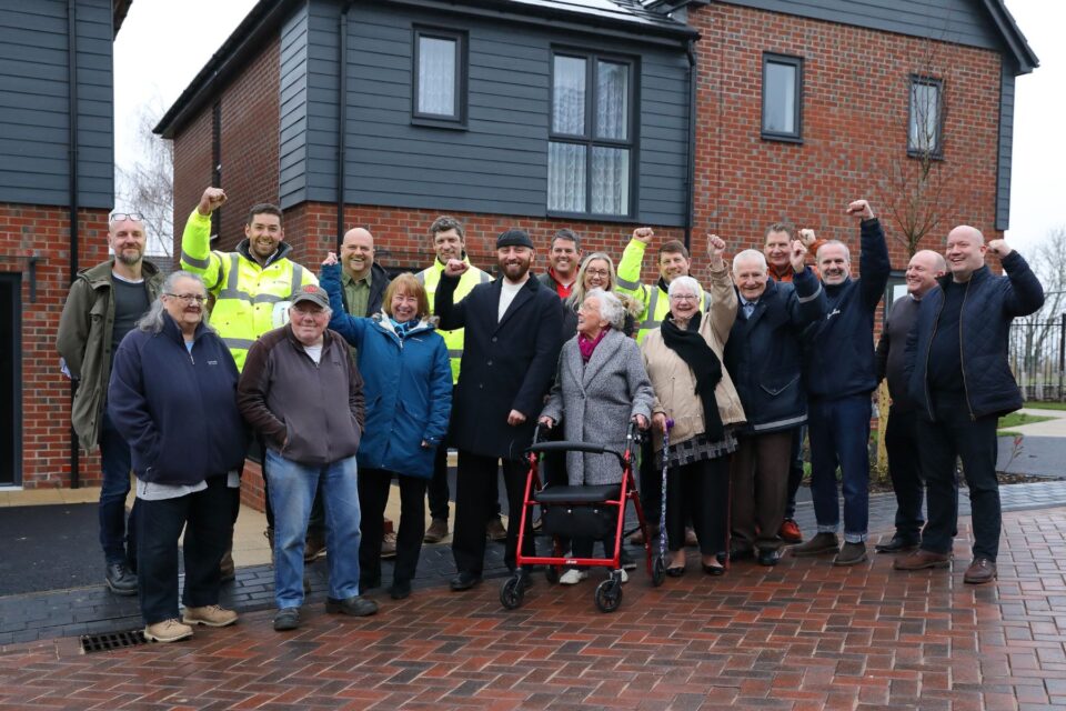 People stood in front of a new house, in a line smiling.