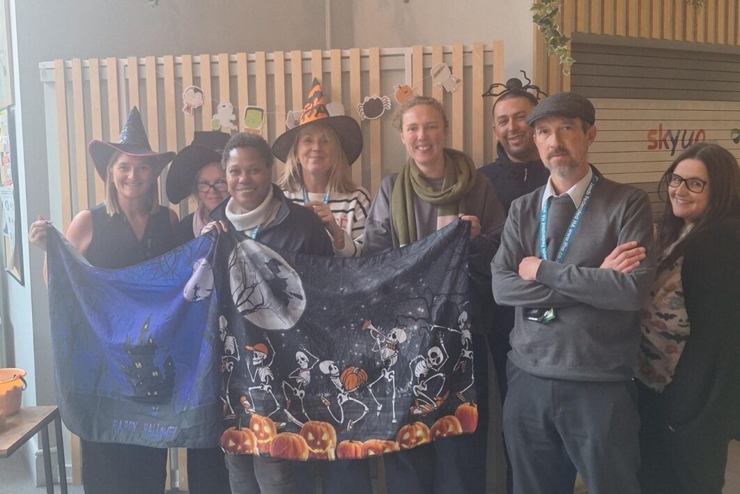 People stood in a row smiling at the camera and holding a halloween-themed banner