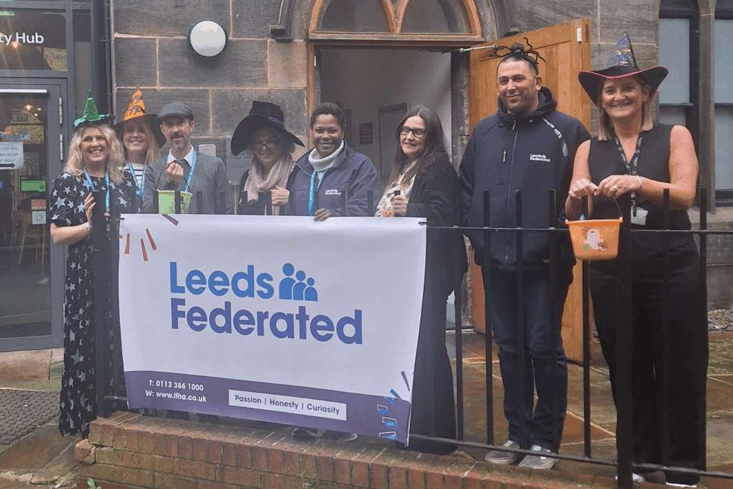 People stood in front of a building. Leeds Federated sign on a railing. People are wearing halloween costumes and witches hats