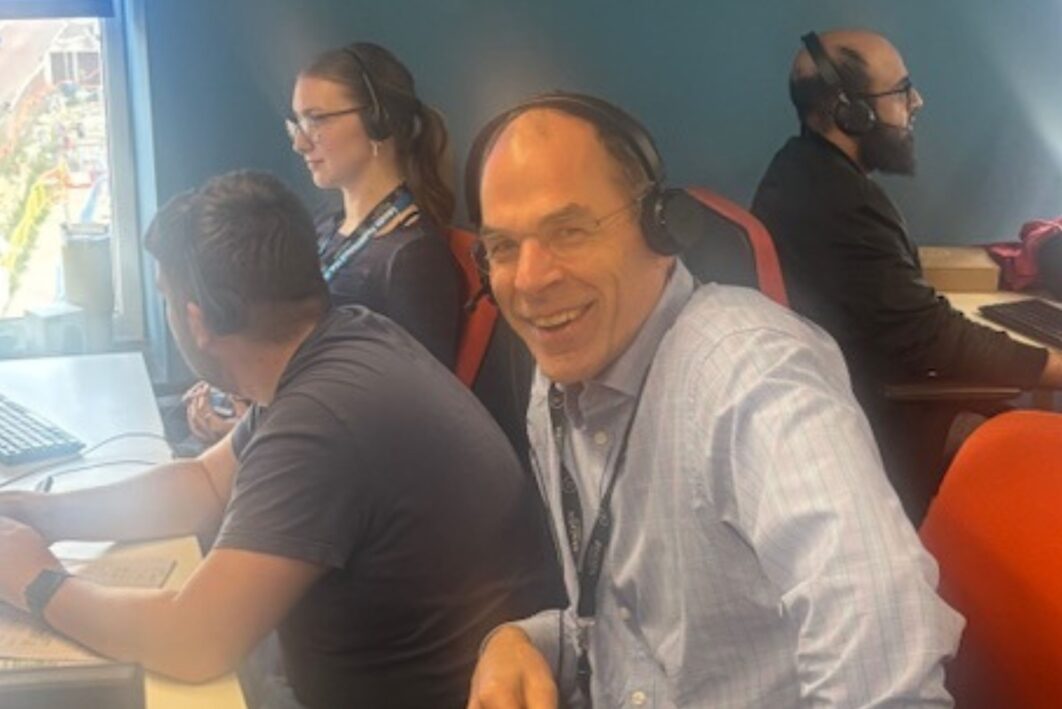 People sat at desks with headsets on. One Person is looking at the camera smiling