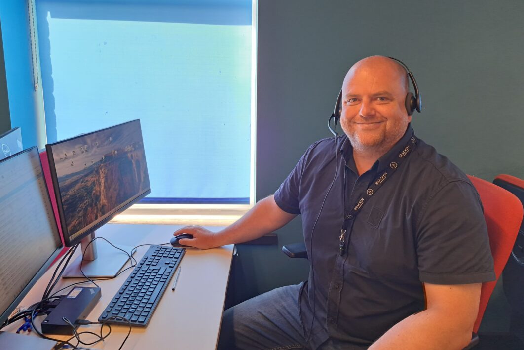 Person sitting at a desks smiling at the camera wearing a headset.