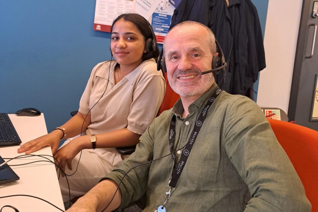 Picture of two people looking at the camera.One of them is wearing a headset.