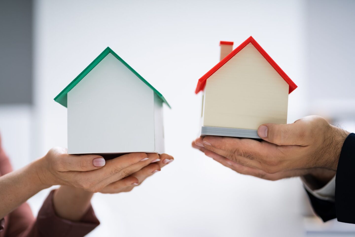 Two people holding two model houses in their hands