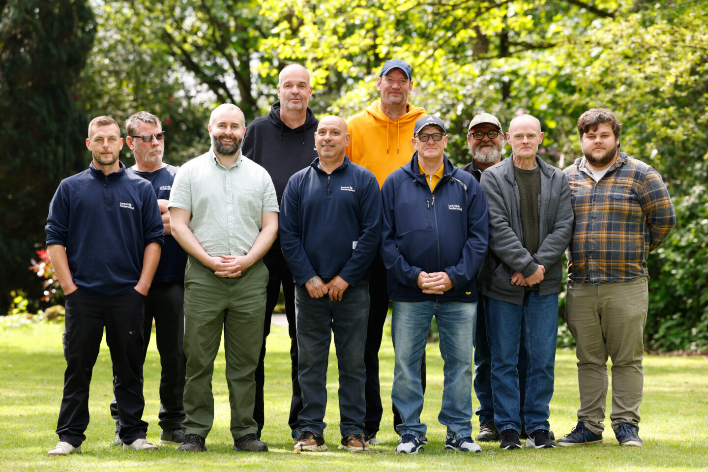 Colleagues from the Community Spaces team standing in a group outdoors surrounded by trees. Everyone is smiling