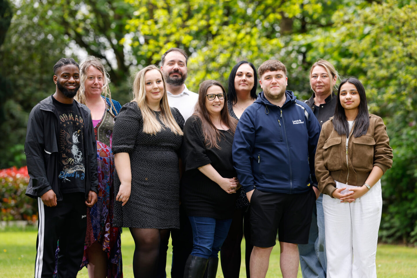 Customer Experience team standing on a lawn together. They are smiling. There are trees in the background.