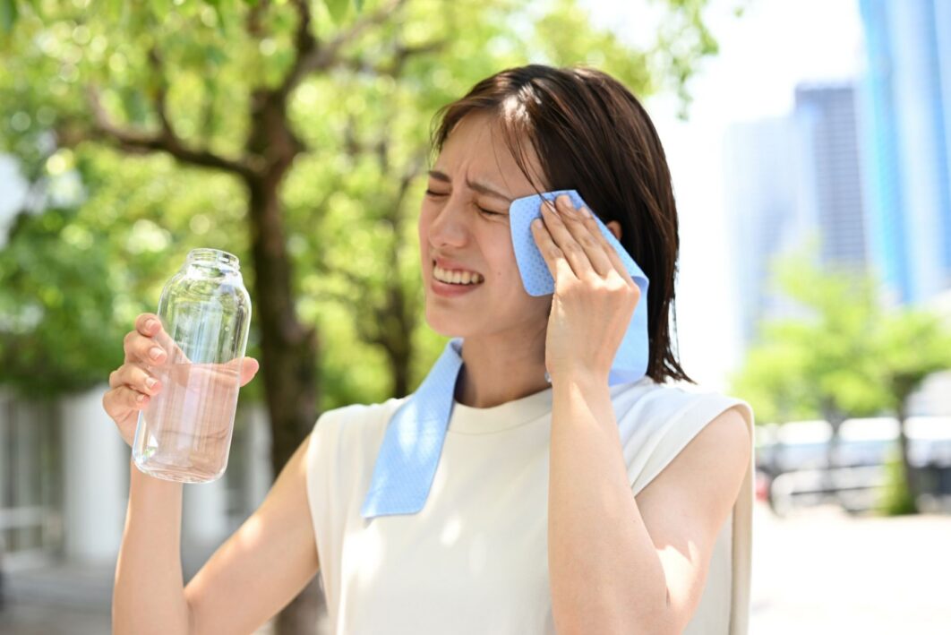Woman drinking water and using wet towel to keep cool