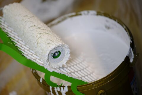 Open can of white paint with roller