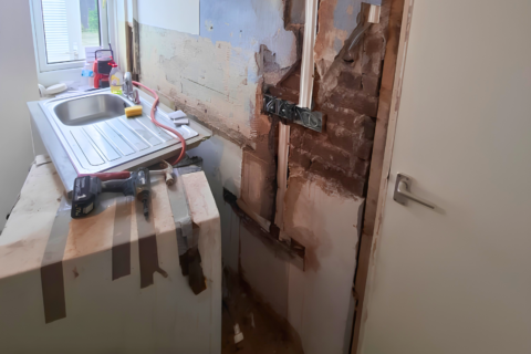 Old kitchen sink and unit being removed. Some plaster has come off the walls around the electric points.