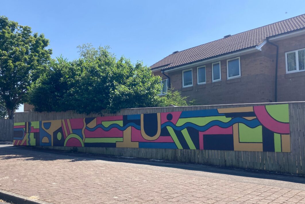 A colourful mural on a wooden fence